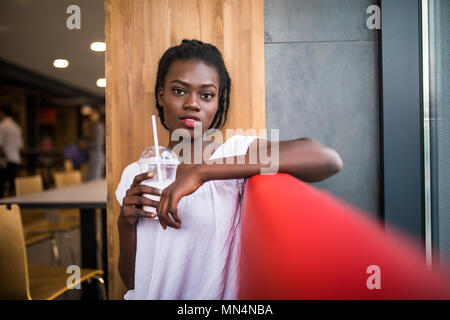 Photo of positive dark skinned afro american female ejoys good rest at coffee shop, drinks beverage. People, leisure and eating concept Stock Photo