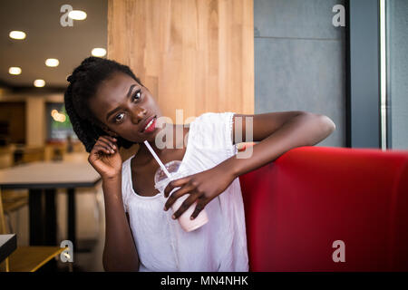 Photo of positive dark skinned afro american female ejoys good rest at coffee shop, drinks beverage. People, leisure and eating concept Stock Photo