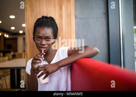 Photo of positive dark skinned afro american female ejoys good rest at coffee shop, drinks beverage. People, leisure and eating concept Stock Photo