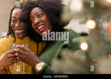 Happy, affectionate women sisters drinking wine next to Christmas tree Stock Photo