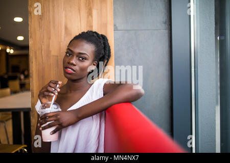 Photo of positive dark skinned afro american female ejoys good rest at coffee shop, drinks beverage. People, leisure and eating concept Stock Photo