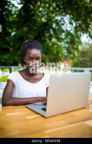 Young afro american black female freelancer working with digital tablet outdoors in street cafe on a sunny day. Stock Photo