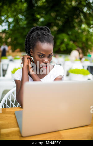 Young afro american black female freelancer working with digital tablet outdoors in street cafe on a sunny day. Stock Photo