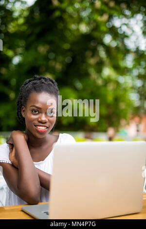 Young black curly female is sitting in street bar and having remote work using laptop Stock Photo
