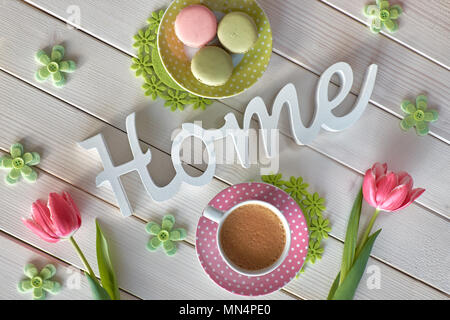 Spring coffee background. The word "Home" made of wood, pink tulips, espresso, macarons and Spring decorations, top view. Stock Photo