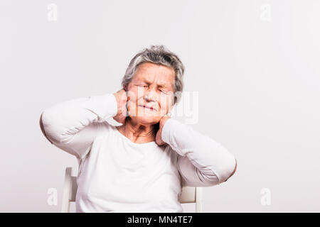 Studio portrait of a senior woman in pain, sitting on a chair. White background. Stock Photo