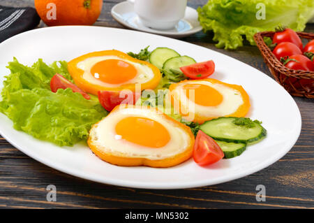 Fried egg in a circle of sweet pepper on a white plate with fresh vegetables on a wooden background. Delicious healthy breakfast. Proper nutrition. Stock Photo