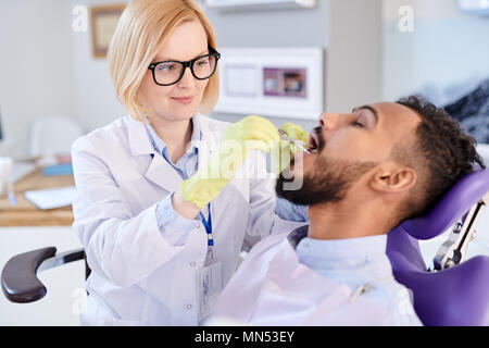Portrait of smiling female dentist examining teeth of young patient sitting in dental chair Stock Photo