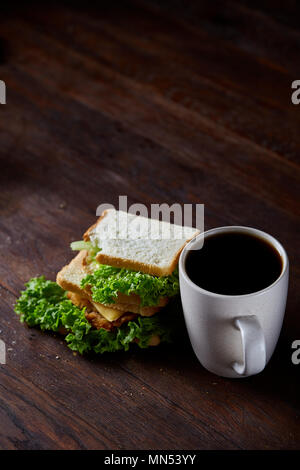 Breakfast table with fresh cheese and lettuce sandwich and black coffee in white ceramic mug on rustic wooden background, close-up, selective focus. B Stock Photo