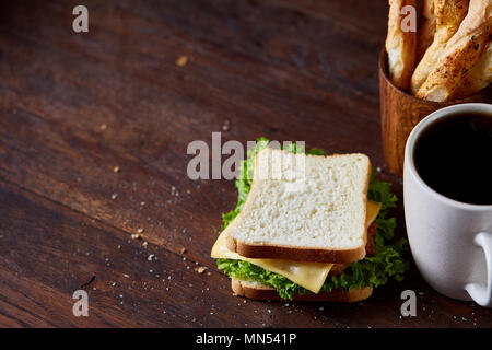 Breakfast table with fresh cheese and lettuce sandwich and black coffee in white ceramic mug on rustic wooden background, close-up, selective focus. B Stock Photo