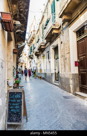 Siracusa, Italy - August 17, 2017: Narrow street with people around in the old town of the historic village of Siracusa in Sicily, Italy Stock Photo