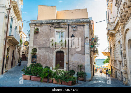 Siracusa, Italy - August 17, 2017: Narrow street with people around with the sea in the background in the old town in Siracusa, Sicily, Italy Stock Photo