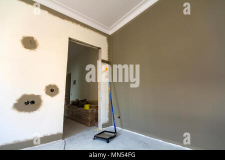 Roller, paint and tools for making repair work in empty apartment room. Construction and renovation concept. Stock Photo