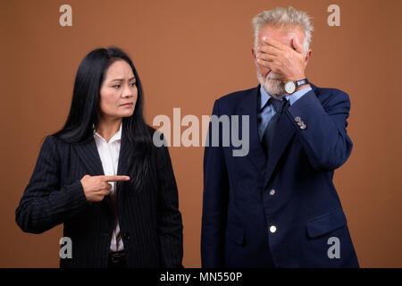 Mature multi-ethnic business couple against brown background Stock Photo