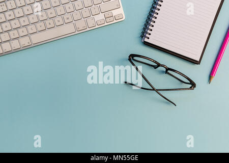 Computer keyboard notebook pencil and eyeglasses on bright blue background Stock Photo