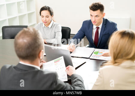 High angle view at business meeting with handsome young man explaining partnership terms to colleagues sitting at table in conference room Stock Photo