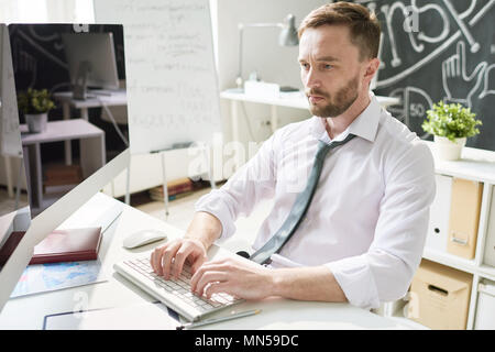 Portrait of handsome bearded businessman sitting at desk in office and using modern computer, typing, copy space Stock Photo