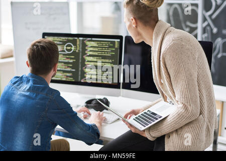 Back view portrait of two contemporary web developers writing code for program using computers in modern office, copy space Stock Photo