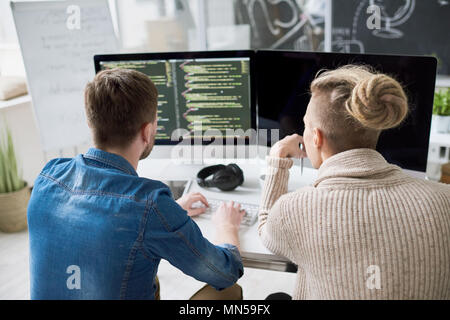 Back view portrait of two contemporary program developers writing code sitting at desk with computer and collaborating on startup project in modern of Stock Photo