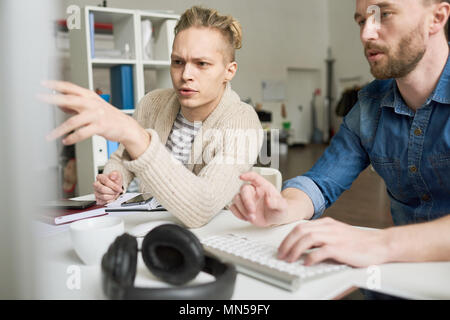 Portrait of two contemporary program developers writing code sitting at desk using computer and collaborating on startup project in modern office, cop Stock Photo