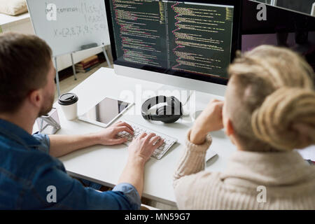 High angle view portrait of two contemporary program developers writing code sitting at desk using computer and collaborating on startup project in mo Stock Photo