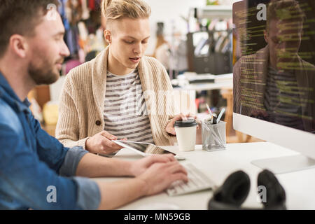 Portrait of creative young man writing code sitting at desk using computer and collaborating with colleague on startup project in modern office Stock Photo