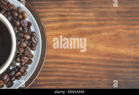 A cup of coffee on a saucer with fried coffee beans, placed on the left. On a wooden background, texture, wallpaper Stock Photo