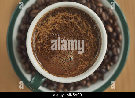 A cup of coffee with thick foam on a saucer with coffee beans Stock Photo