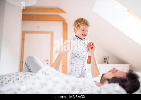 Mature father with a toddler boy having fun in bedroom at home at bedtime. Paternity leave. Stock Photo