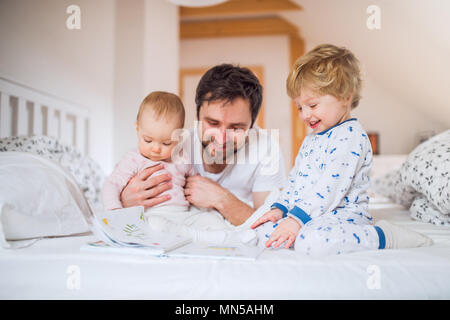 Handsome father with toddler children in bedroom at home, reading stories at bedtime. Paternity leave. Stock Photo