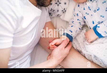 Unrecognizable father holding hand of a sleeping toddler boy lying in bed at home. Paternity leave. Stock Photo