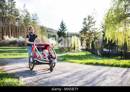 A father with two toddler children sitting in jogging stroller on a walk outside in spring nature. Stock Photo