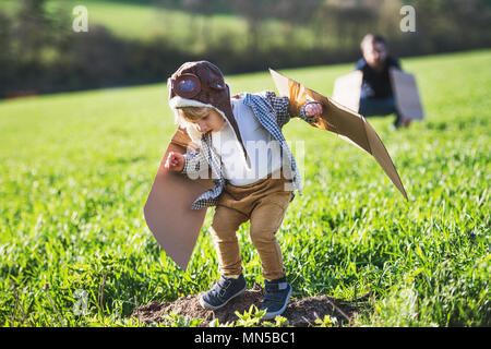 Happy toddler boy with hat, goggles and wings playing outside with unrecognizable father in spring nature. Pilot and flying concept. Stock Photo