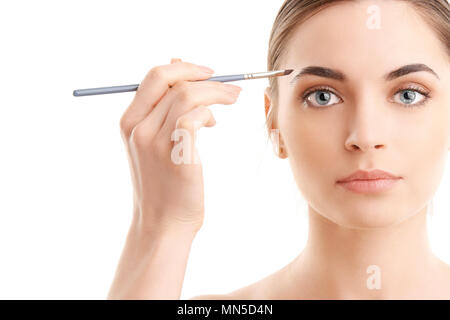 Studio shot of a beautiful young woman applying makeup to her eyebrow while standing at isolated white background with copy space. Stock Photo