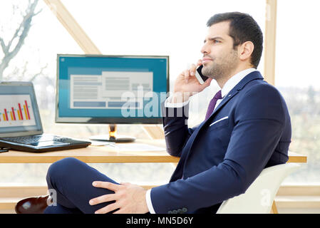 Portrait of young financial businessman analyzing financial data and consulting with his client on mobile phone. Stock Photo