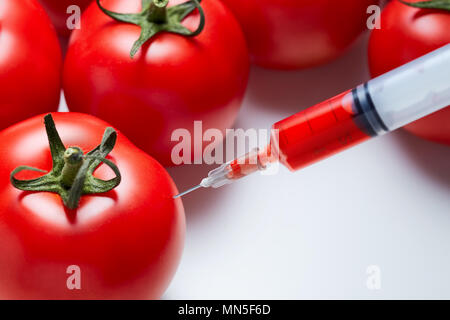 Close-up shot of a syringe injecting a red liquid to fresh red tomatoes. Concept of genetic modification. Stock Photo