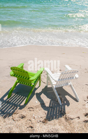 A pair of adirondack chairs on the beach facing the ocean.  They are empty. Stock Photo