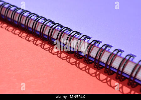 A closed, purple, spiral bound notebook on a red background with the shadow of the spiral Stock Photo