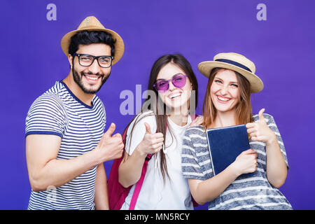 Group of happy smiling students dressed in t-shirts, hats and eyeglasses before purple background Stock Photo