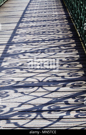 Shadows cast by the elaborate filigree ironwork of the balustrade, on to the wooden decking of the footbridge over the river Ill. Stock Photo