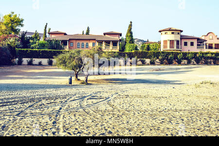 Daylight view to buildings near beach with car tires traces on sand. Bright blue clear sky. Negative copy space, place for text. Limassol, Cyprus Stock Photo