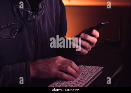 Computer hacker using smartphone device in dark interior, low key with selective focus Stock Photo