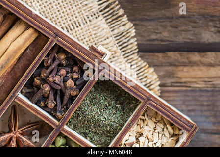 Box with variety of dried spices, such as ginger, mint, clove, chili flakes, cardamon, star anise, cinnamon sticks on dark rustic wooden background Stock Photo