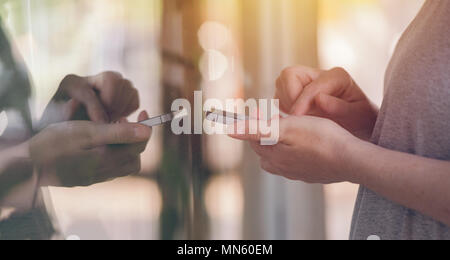 Using mobile phone in front of store shop window. Female hands holding smartphone device and using app to check the prices. Selective focus. Stock Photo