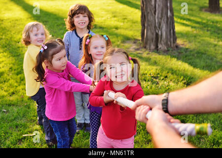 a group of small preschool children play a tug of war in the park.  Stock Photo