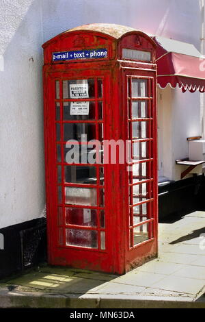 Padstow, Cornwall, UK - April 11 2018: Old traditional British red telephone box with flaking paint, in need of restoration, on a sunny street. Stock Photo