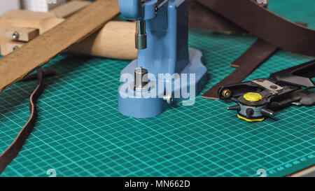 Tools tanner on desktop in workshop. Close-up. Punch, riveter, ruler and pieces of leather lie on carpet for cutting. Stock Photo