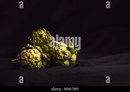 several fresh green artichokes on a black background Stock Photo