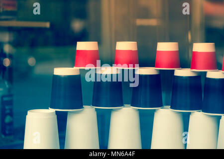Disposable paper cups in the cafe showcase. Coffee to go. Red, black and white ecological cups of different sizes and shapes pyramid upside down behin Stock Photo