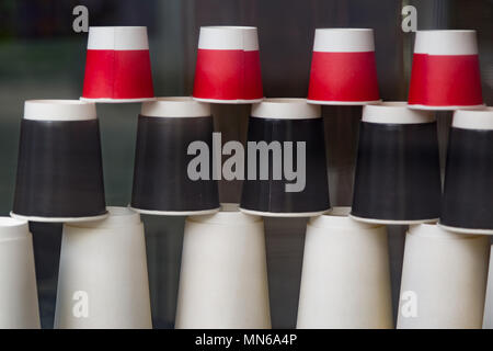 Disposable paper cups in the cafe showcase. Coffee to go. Red, black and white ecological cups of different sizes and shapes pyramid upside down behin Stock Photo
